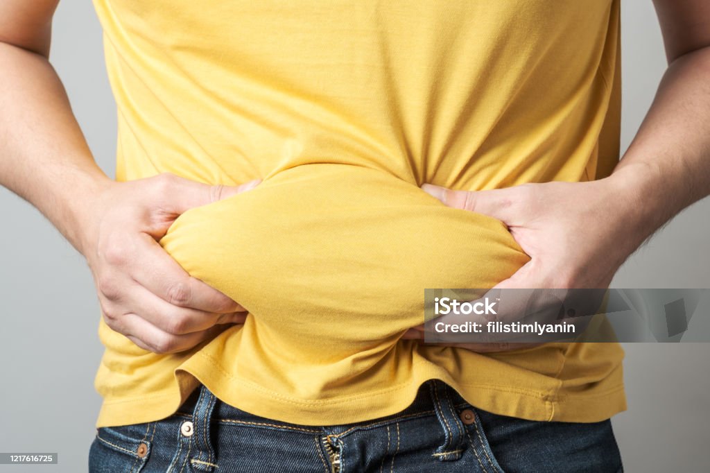 Close up of overweight obese man's hand holding his big belly isolated over gray background